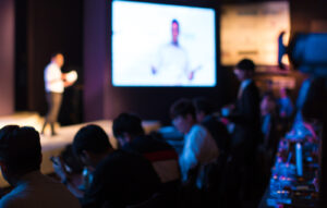 A,Presenter,With,Hands,Up,Giving,Presentation,While,Audience,People